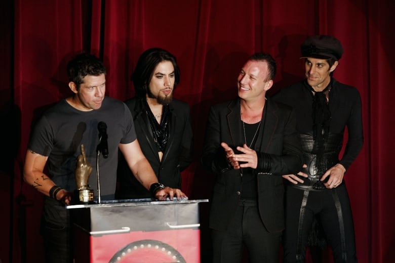 Four men in dark clothing are shown standing near a podium.