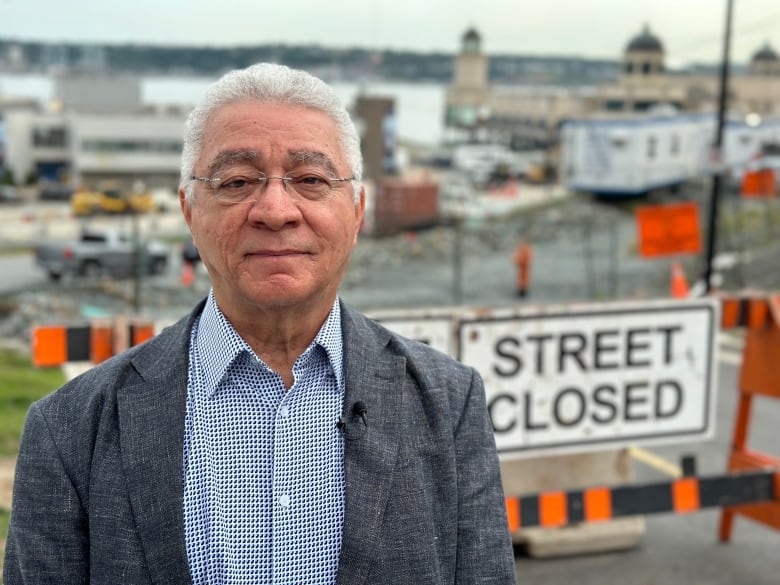 A man stands by a street closure sign with the Halifax Harbour in the background.