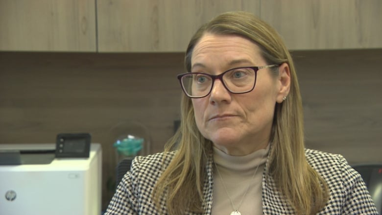 A lady in glasses is interviewed in an office.