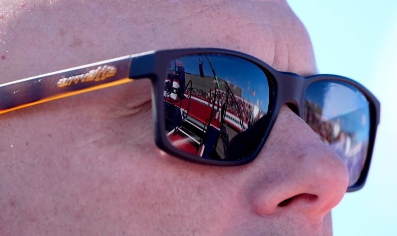 A close-up of the upper half of a man's face, focusing on the reflection in his sunglasses. 