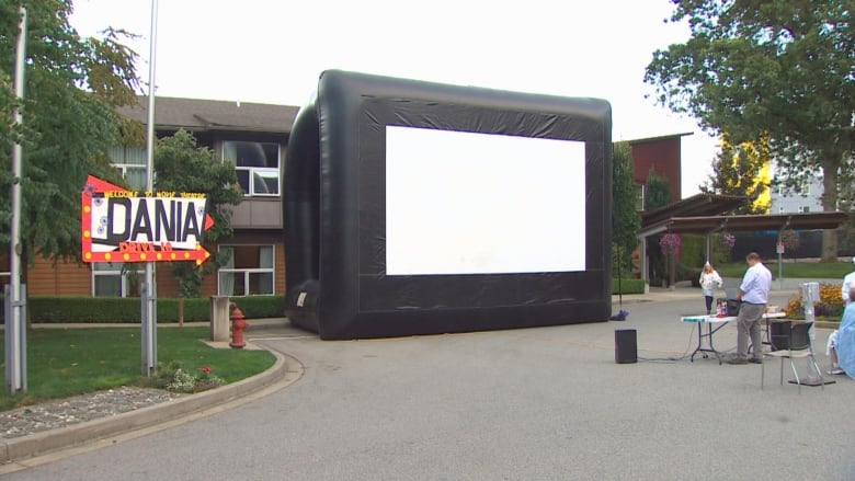 A sign reading 'Dania Drive-In' points to a large screen that looks like a giant TV screen outdoors.