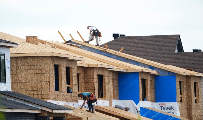 Two men work on the rooftops of houses under construction.