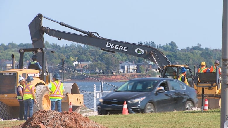 Workers standing around backhoe.