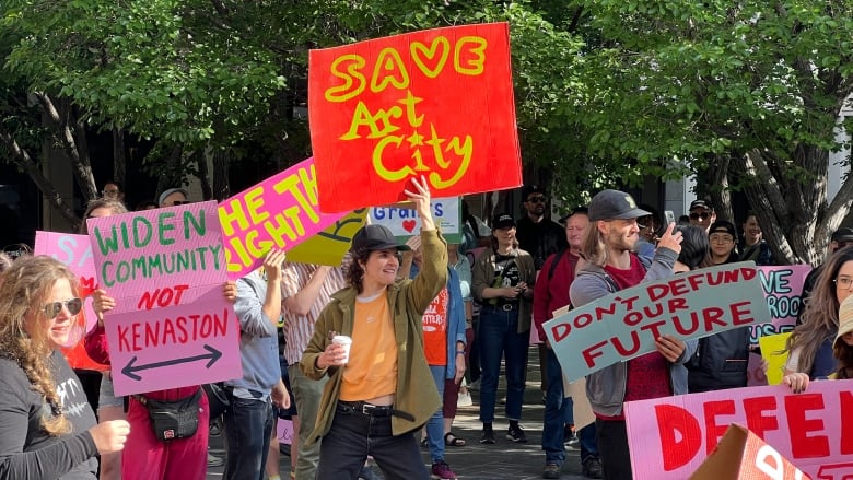 A crowd of people are standing in a court yard holding signs. One reads 