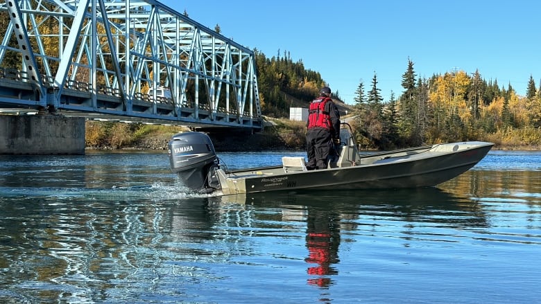 A police officer in boat on river next to a bridge looks into the water. 