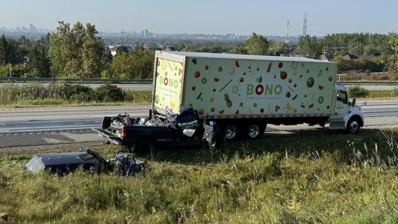 A pickup truck that has crashed into the back of a transport truck on a highway on a summer morning.