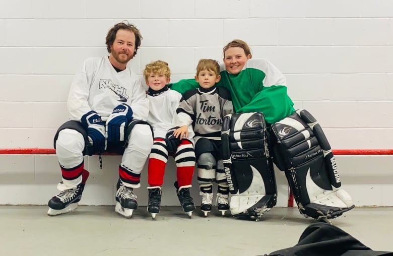 A family of four is seen wearing hockey attire, sitting on a bench.