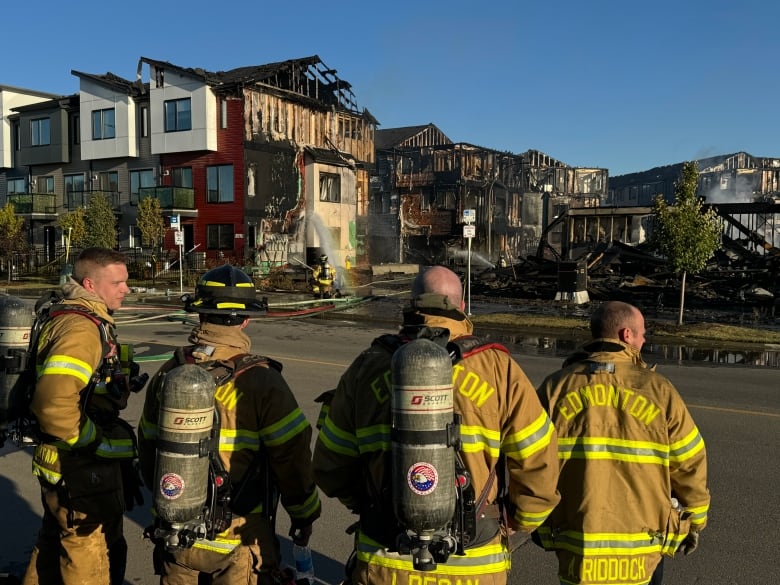 Four firefighters look towards a burned building. 