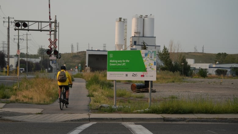 A person wearing yellow cycling on a sidewalk next to a green sign that reads 