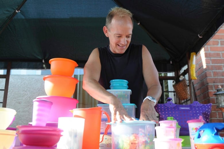 A person in a black tank top looks enthusiastic while stacking Tupperware on a table.