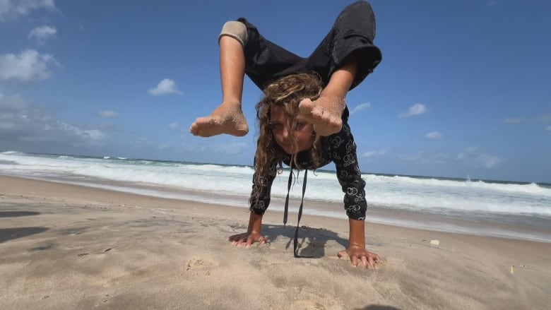 A child stands on his hands by the sea.