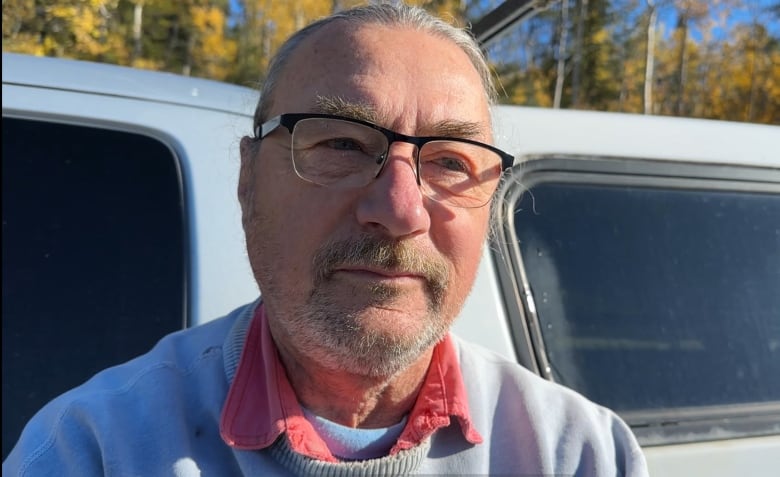 A man with glasses stands in front of a pickup truck.