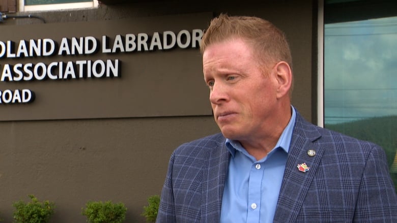 A man wearing a plaid blue blazer stands outside an office building.