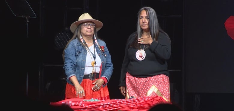 Two women stand on a stage while looking at a red cloth. 