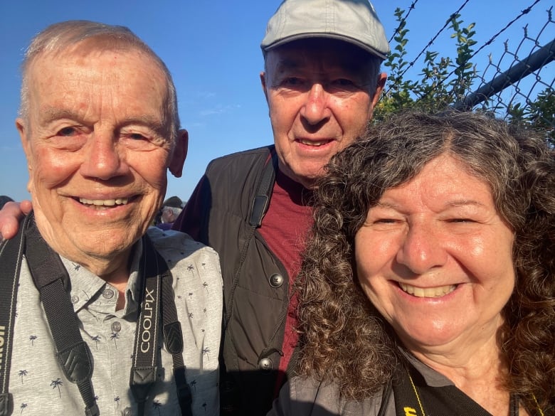 A selfie showing three people outdoors by a fence.