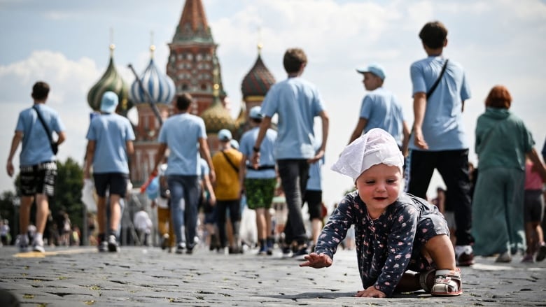 A child crawls on a street while people walk in the background.