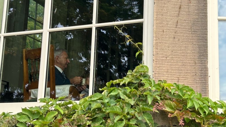 A man seen through a window holding a mug