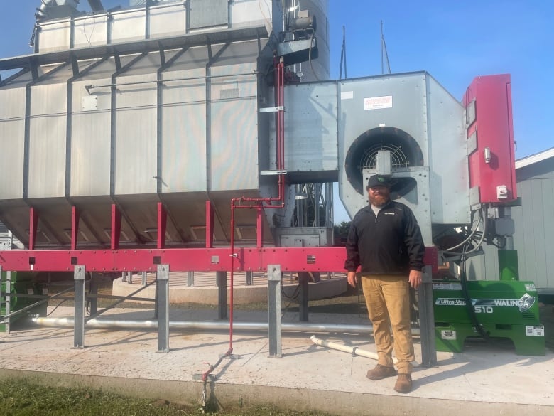 A man stands next to a large machine that dries crops 