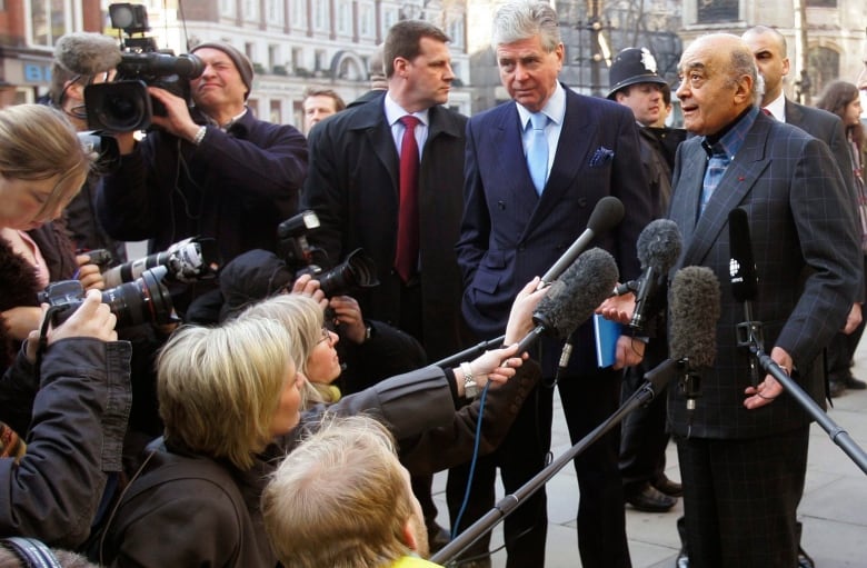 A person speaks into microphones held by several members of the media.