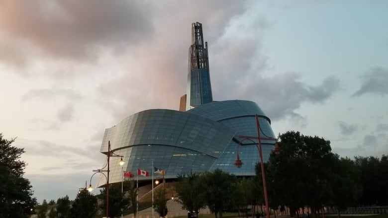 A curved glass building with a spire against a setting sun sky