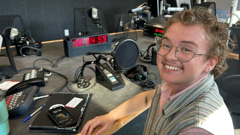 A person with curly hair and glasses sitting in a radio studio.