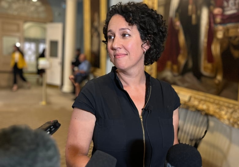 A woman with dark curly hair stands in front of microphones.