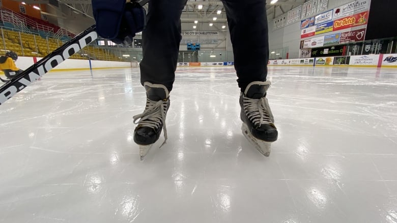 A person stands on skates and holds a hockey stick. 