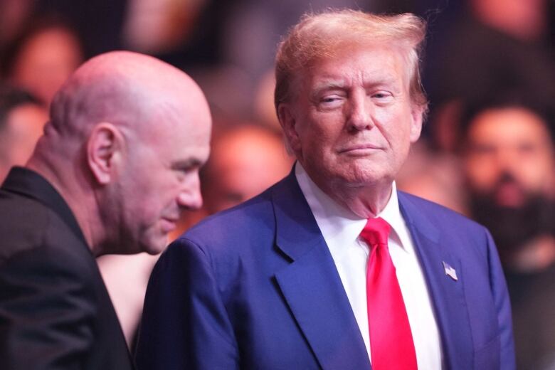 Donald Trump wears a suit as he stands next to a bald men dressed in black.