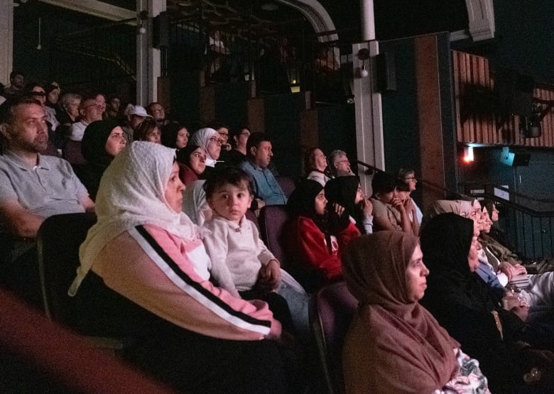 Several dozen people sit in four rows of a theatre 