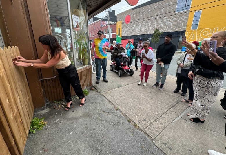 Woman places brass plaque on a wooden gate as people stand near her taking photos.