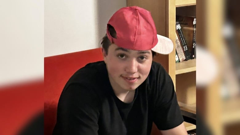 A teenage boy wearing a red cap sideways and a black t-shirt. 