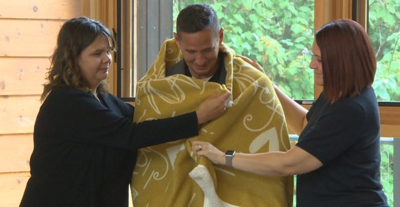 Two women wrap a man in a blanket.