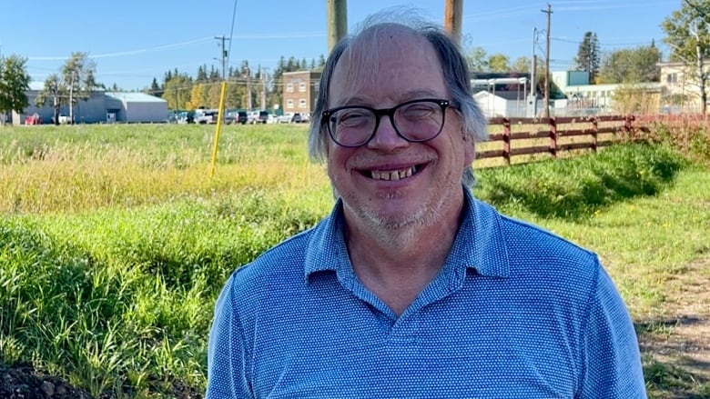 A man stands in front of a field, smiling.