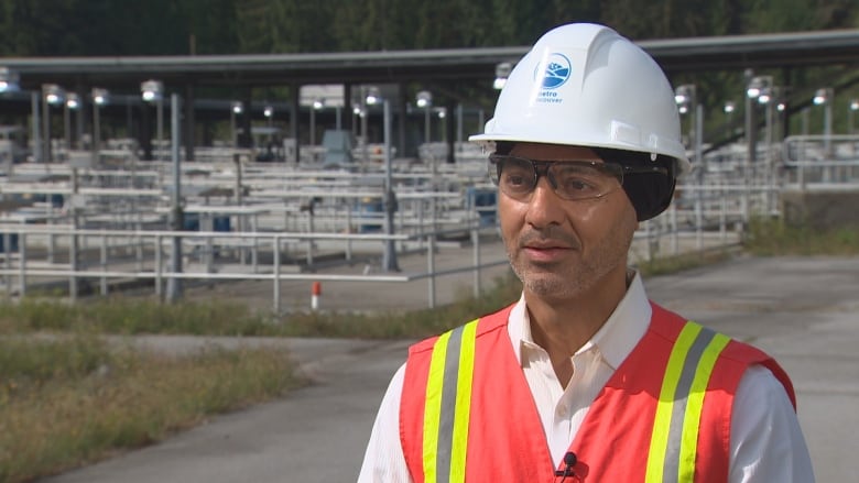 Inder singh standing in front of water treatment plant. He is a South Asian man wearing a hard hat and a high-vis vest.