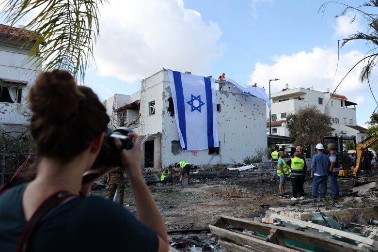 A woman takes a photograph on an Israeli flag deployed on the wall of a damaged building.