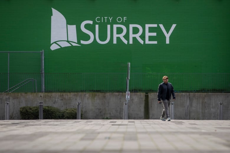 A man walks past a green sign that reads 'City of Surrey'.