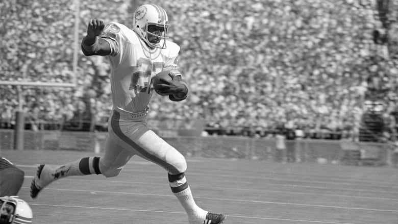 A running back wearing number 22 runs with the ball in his left hand during a game inside a stadium filled with fans.