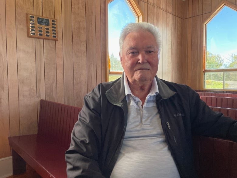 A man with white hair sits in a wooden church. 