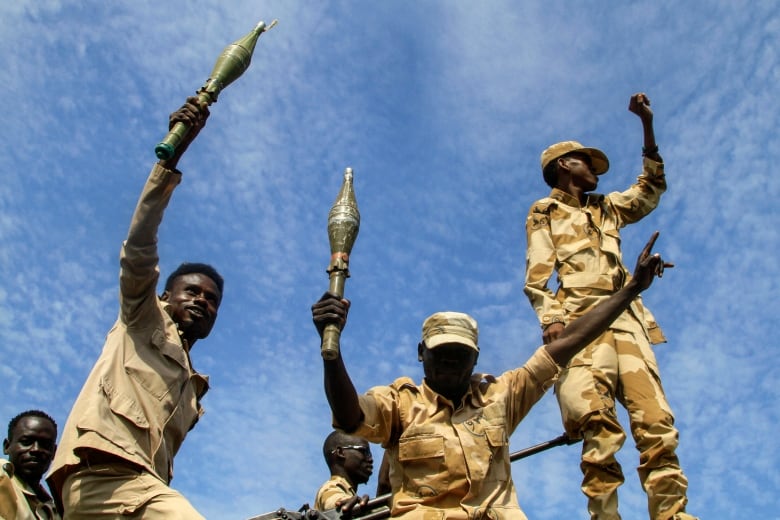 Men in khaki camouflage hold weapons aloft, seemingly in celebration.