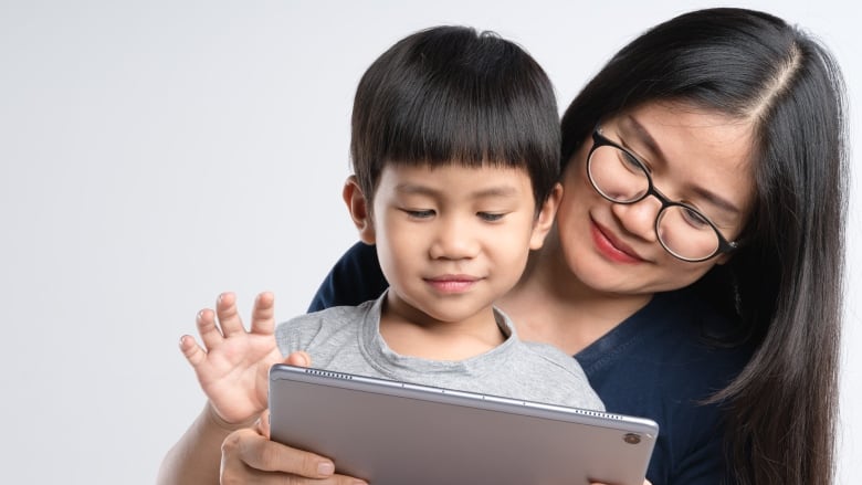 A mother is holding a boy child and they are looking at an iPad together. 