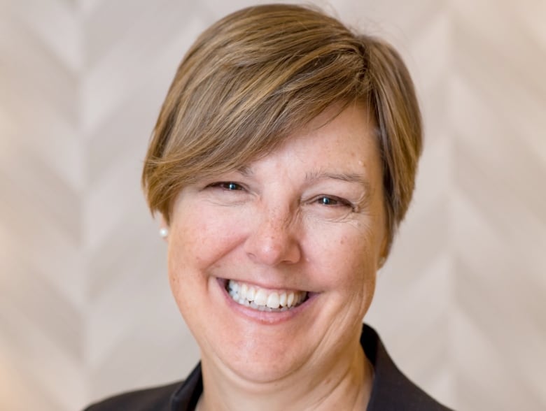 A headshot of a woman with dark blonde short hair, wearing a blazer and smiling at the camera. 