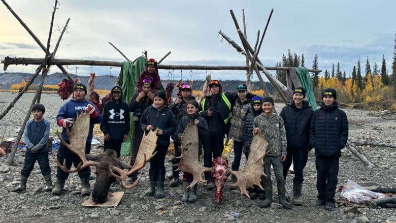 A group of young people stand outside posing with two moose heads.