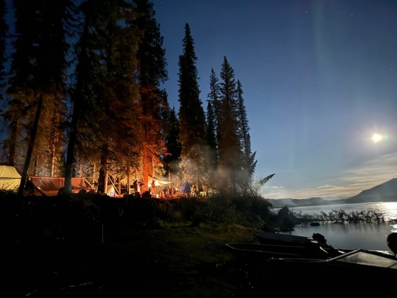 A campsite aglow with firelight beside a river.