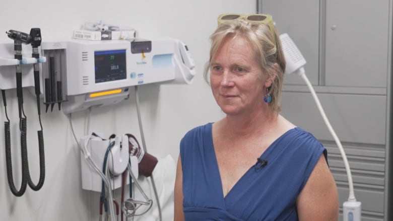 A woman wearing a blue top smiles in a hospital room.