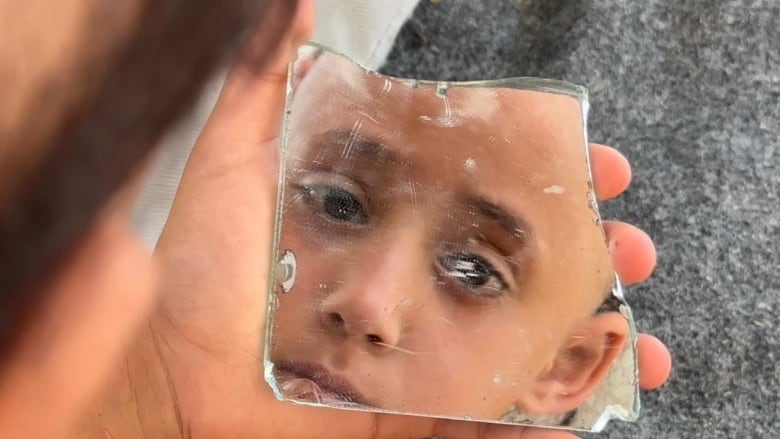 A girl looks at herself in a broken piece of a mirror.