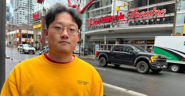 A man in a yellow shirt stands in front of a movie theatre. 