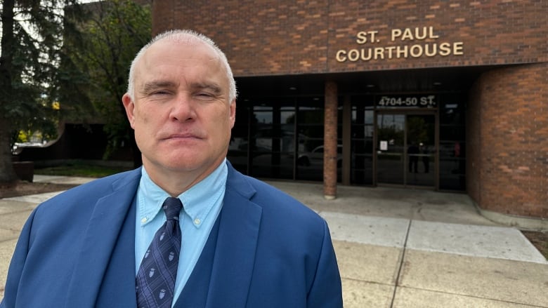 A man in a blue suit stands outside a brick courthouse.