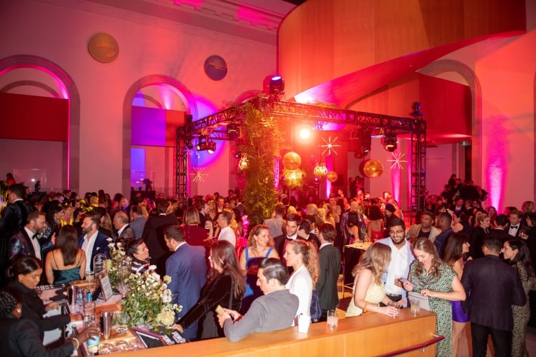 AGO's Art Bash gala in 2022, which had the theme All Out!, marking return of the event post-pandemic. You can see dozens of formally dressed people at the large room with a bar and colourful lights 