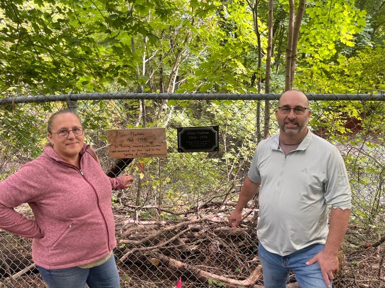 A man and woman standing in a forest next to two plaques. 