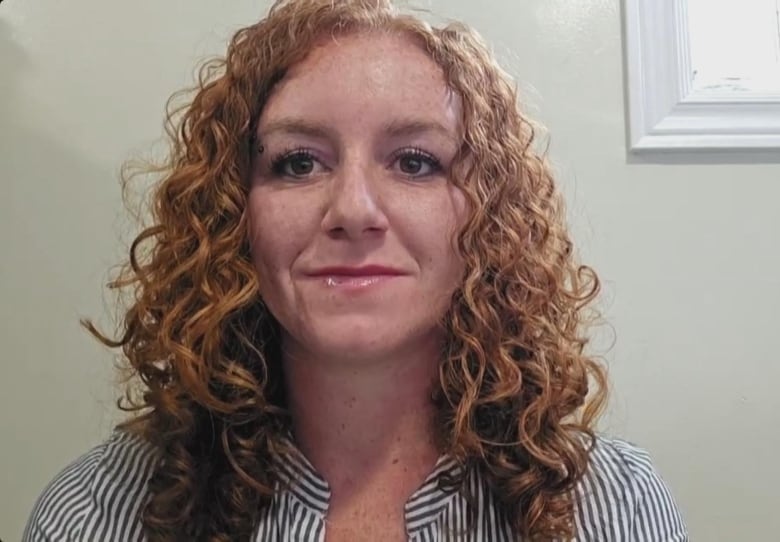 A woman sits in a striped blue shirt. She has curly red hair.